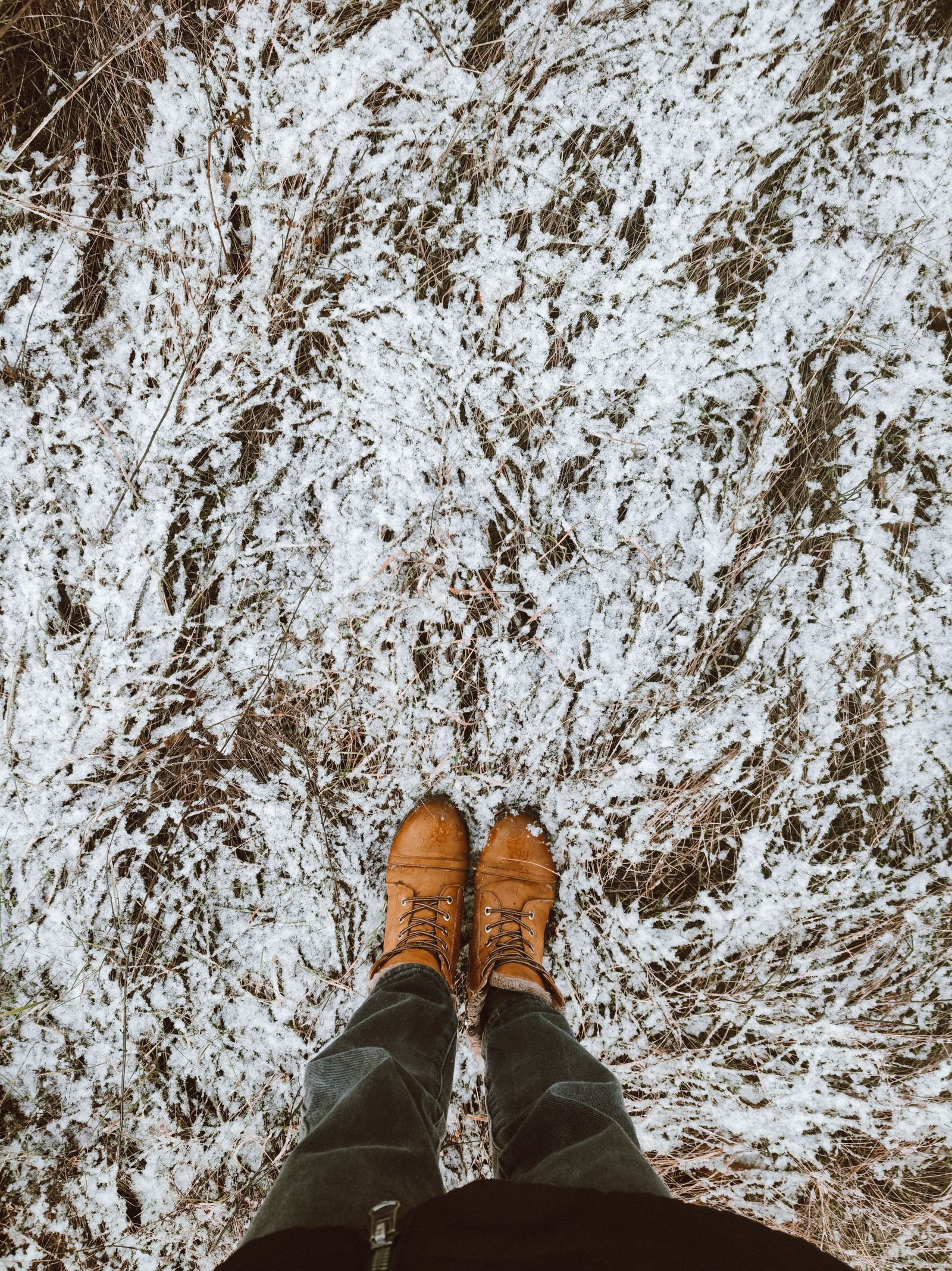 Top-down view of brown boots standing on frost-dusted grass