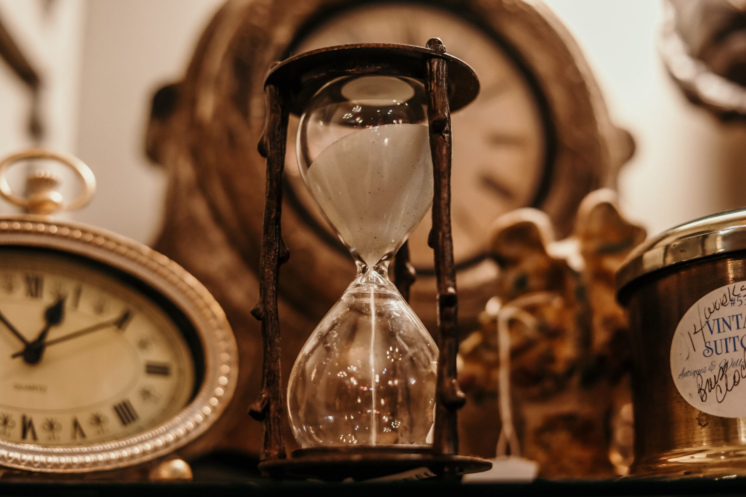 Hourglass with pale sand on a shelf beside an antique clock