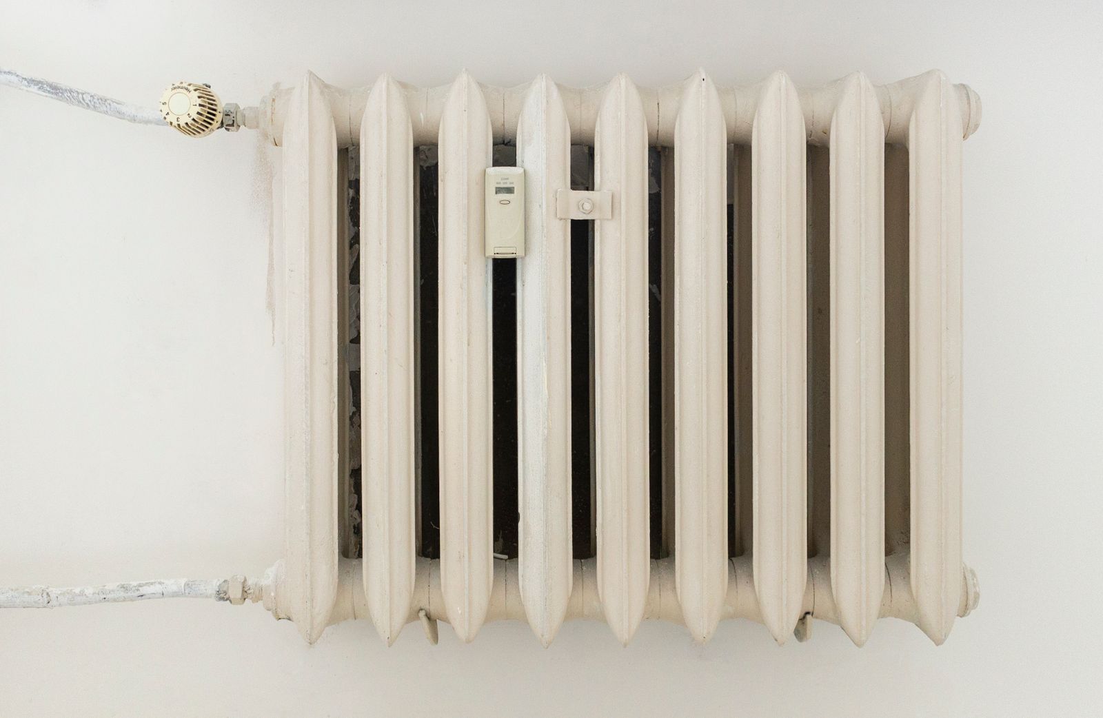 A white cast-iron radiator with a small meter attached, mounted on a white wall