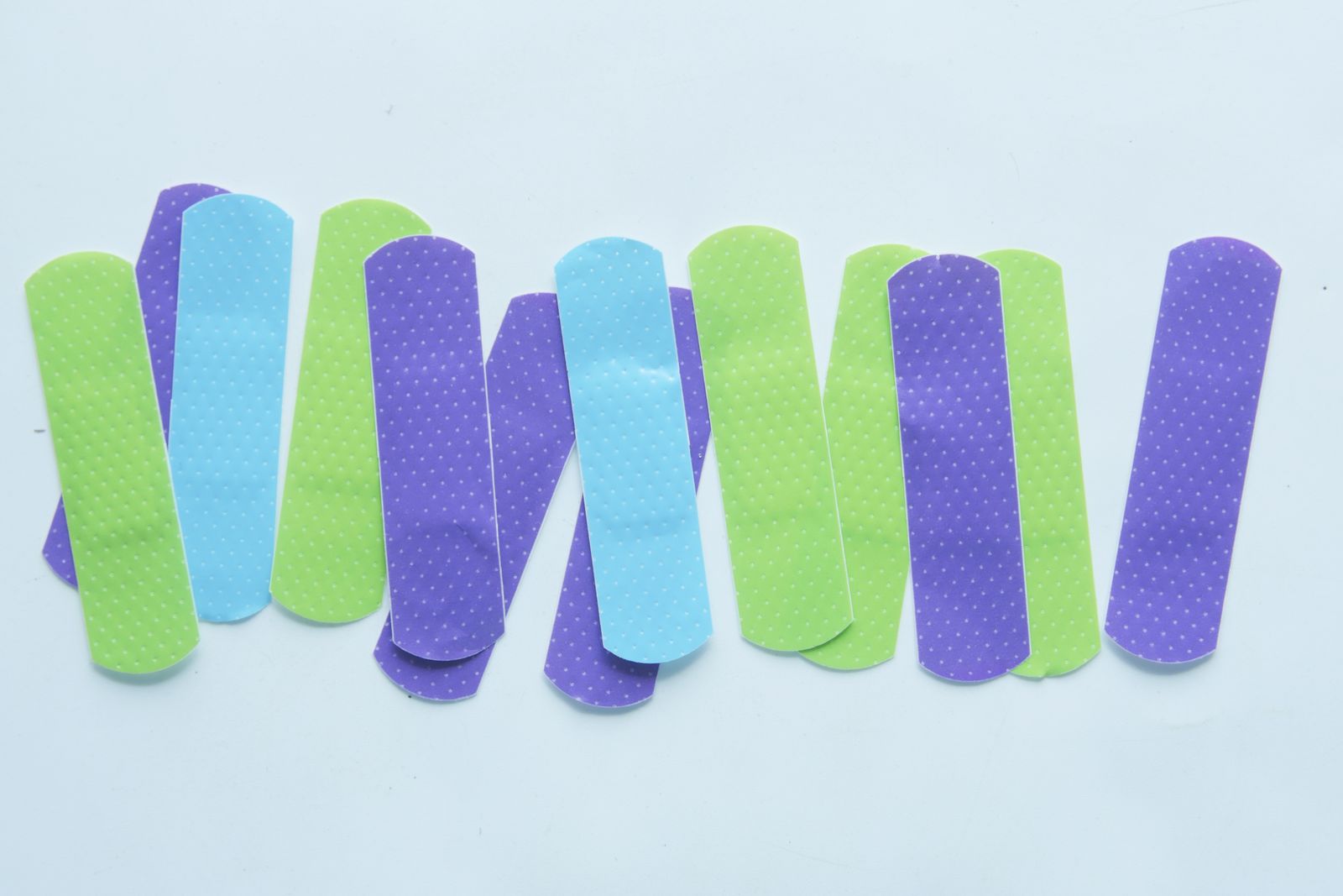 A row of green, blue and purple adhesive bandages laid on a pale blue background