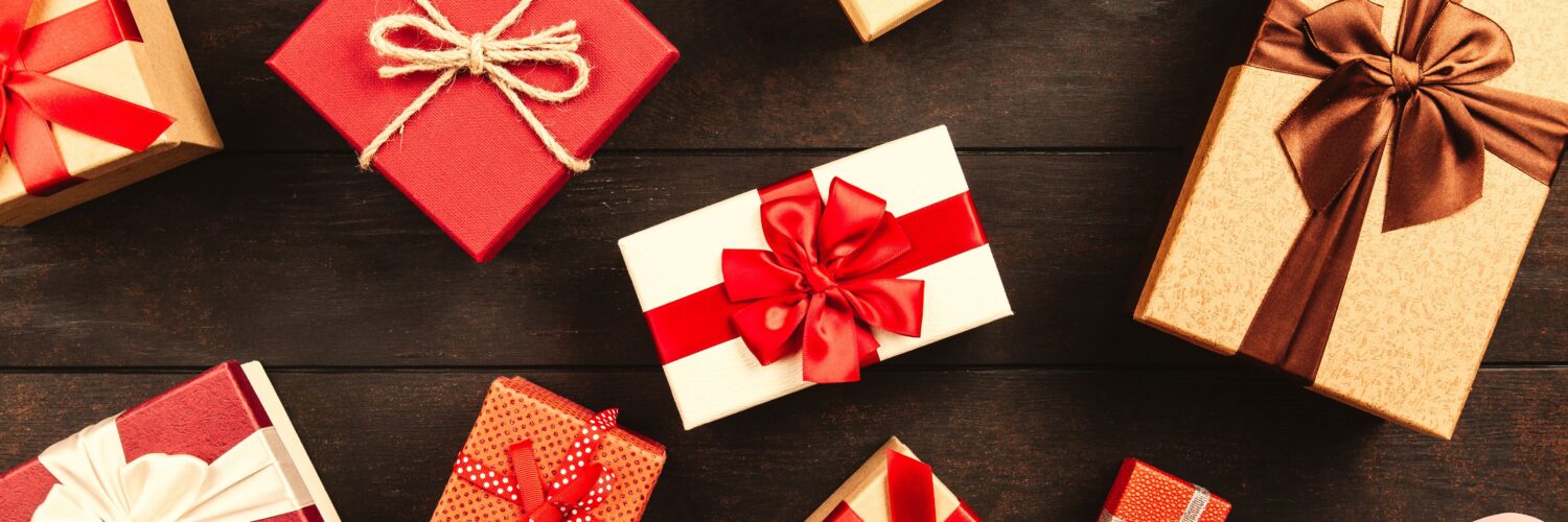 Wrapped gift boxes tied with red, white and brown ribbons and twine, laid out on a dark wooden table