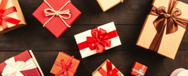 Wrapped gift boxes tied with red, white and brown ribbons and twine, laid out on a dark wooden table