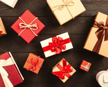 Wrapped gift boxes tied with red, white and brown ribbons and twine, laid out on a dark wooden table