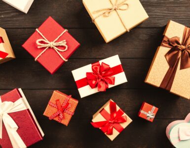 Wrapped gift boxes tied with red, white and brown ribbons and twine, laid out on a dark wooden table