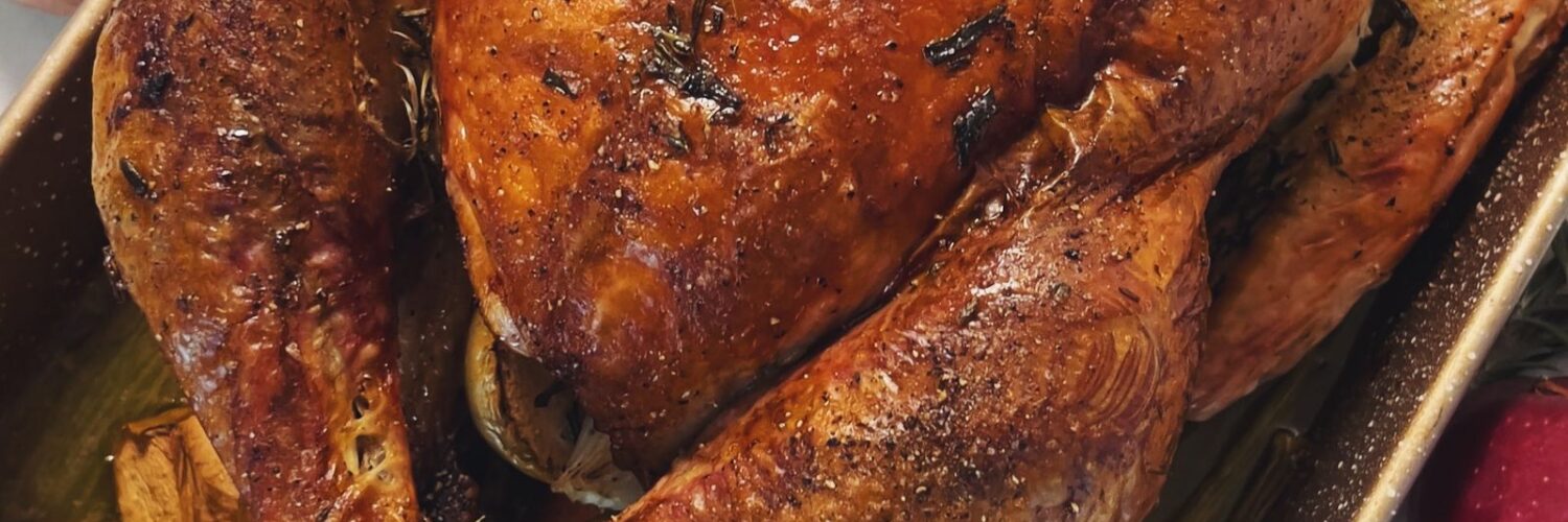 A roasted turkey with a deep brown skin in a rectangular baking pan, seen from above, with green beans and mashed potatoes beside it