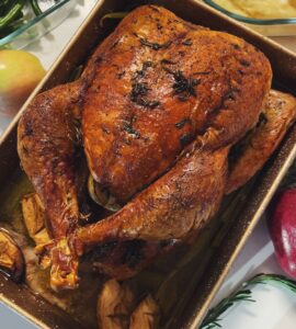 A roasted turkey with a deep brown skin in a rectangular baking pan, seen from above, with green beans and mashed potatoes beside it