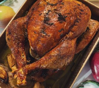 A roasted turkey with a deep brown skin in a rectangular baking pan, seen from above, with green beans and mashed potatoes beside it