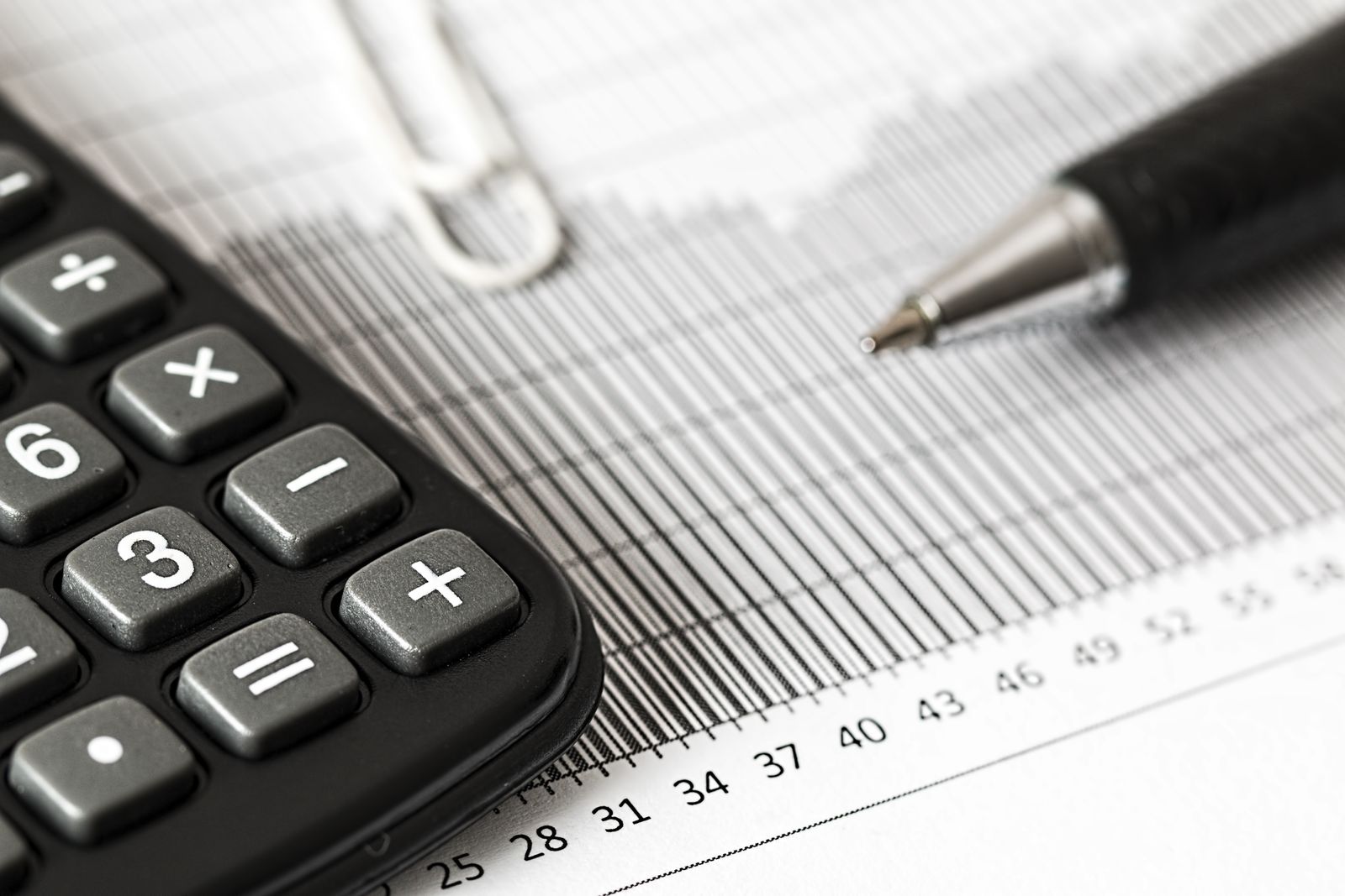 Close-up of a black calculator and a ballpoint pen on a printed bar chart