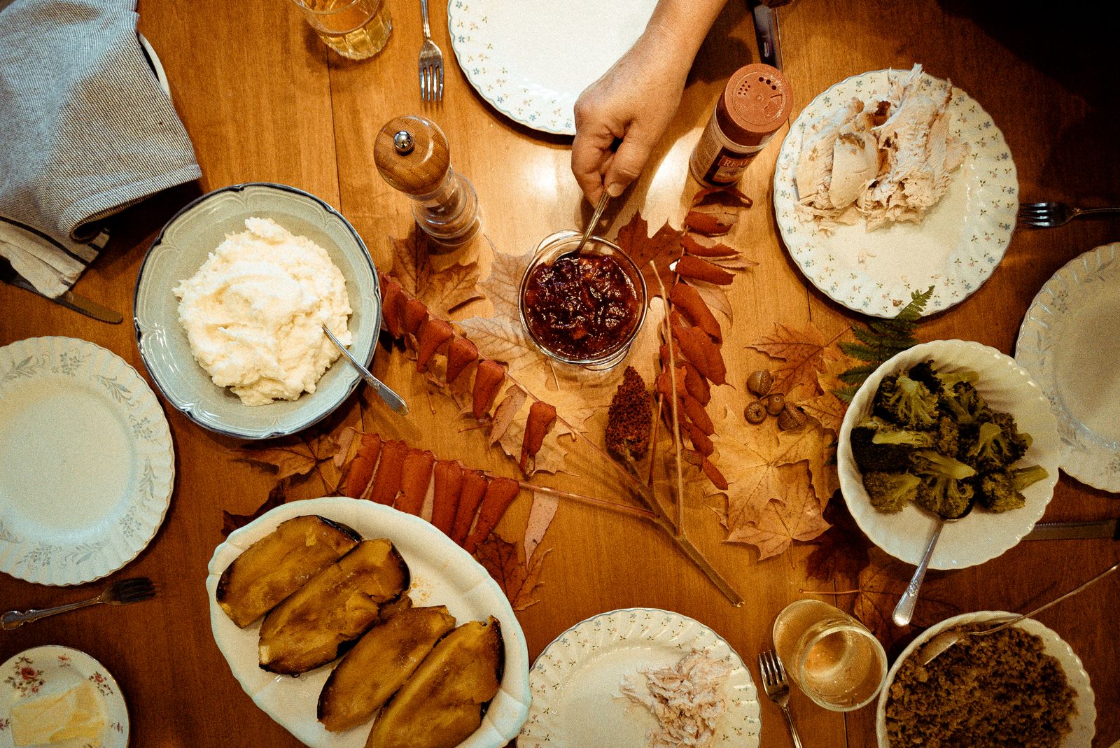 Bowls of mashed potatoes, cranberry sauce and sprouts on a wooden table among autumn leaves