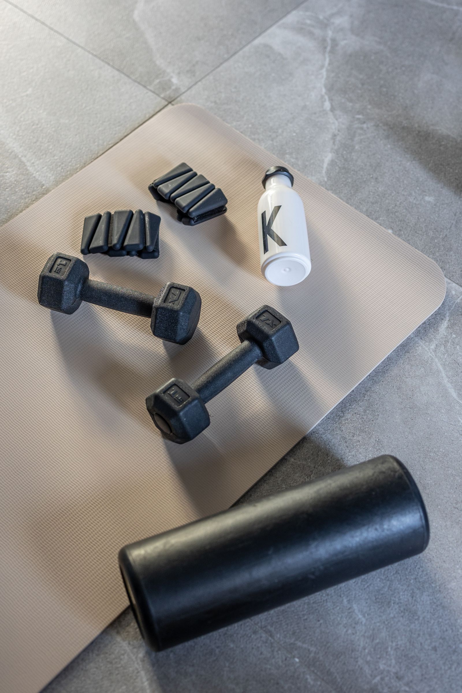 Two dumbbells, a foam roller and a water bottle on a beige yoga mat
