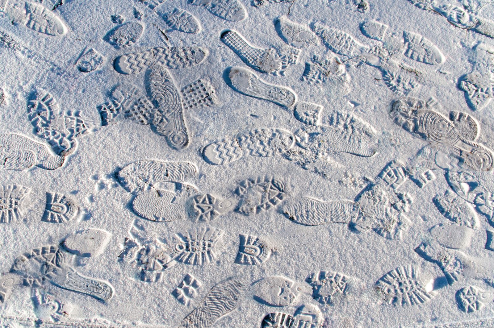 Overlapping boot and shoe sole prints pressed into packed snow