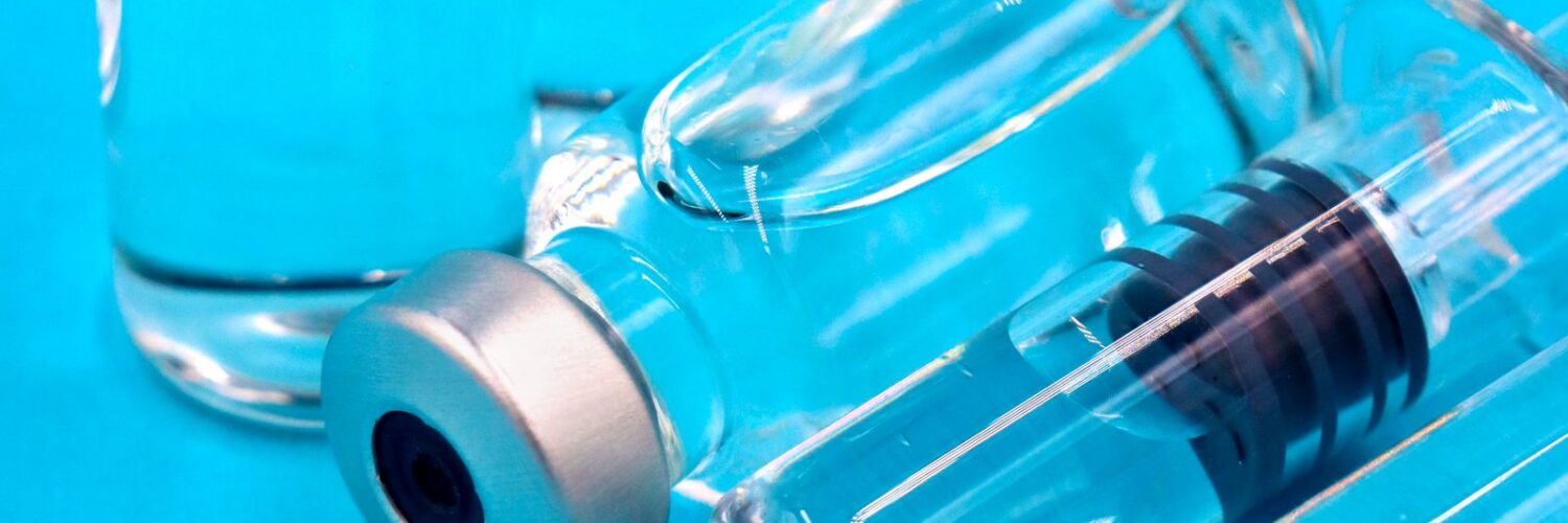 Two clear glass vials with silver caps and a prefilled syringe lying on a bright blue surface