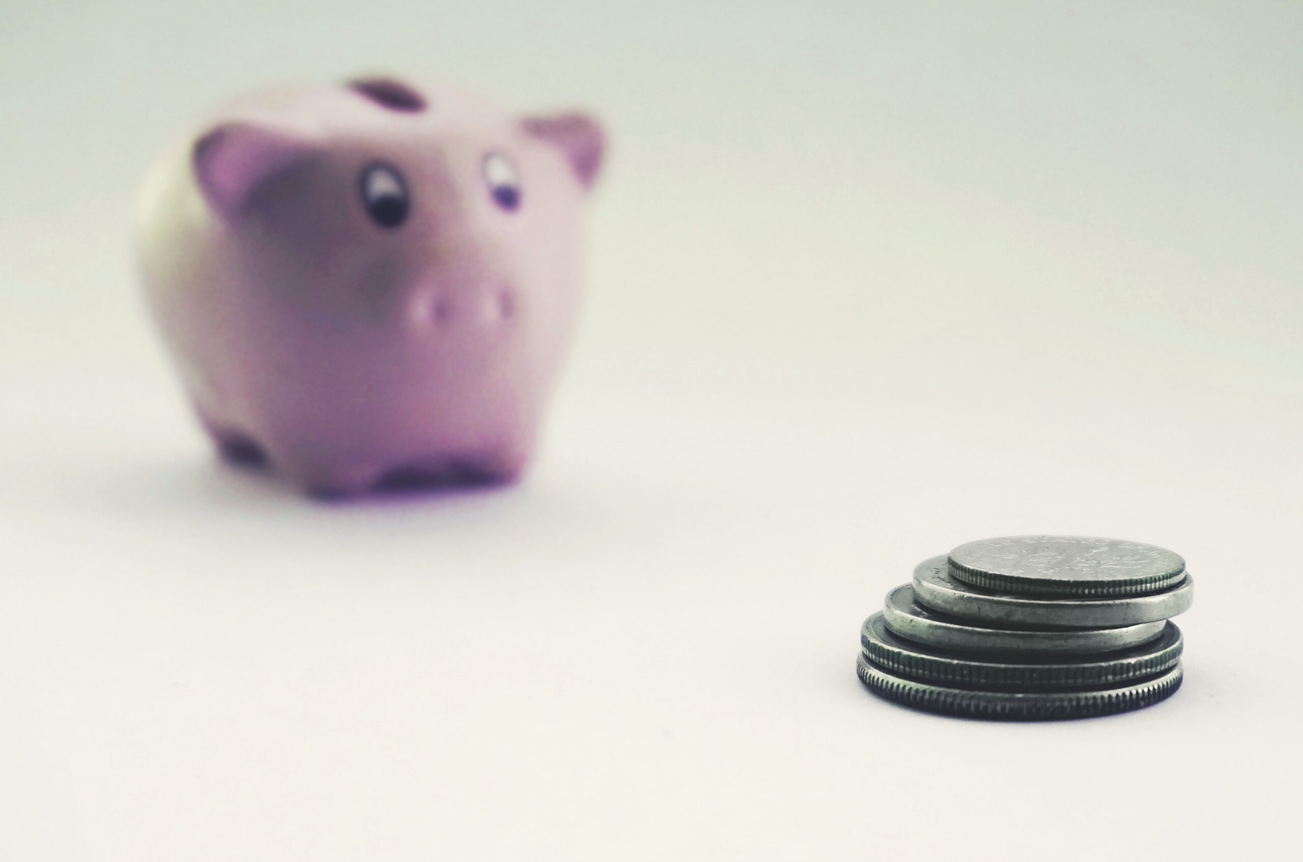 Pink piggy bank blurred behind a small stack of coins on a white surface