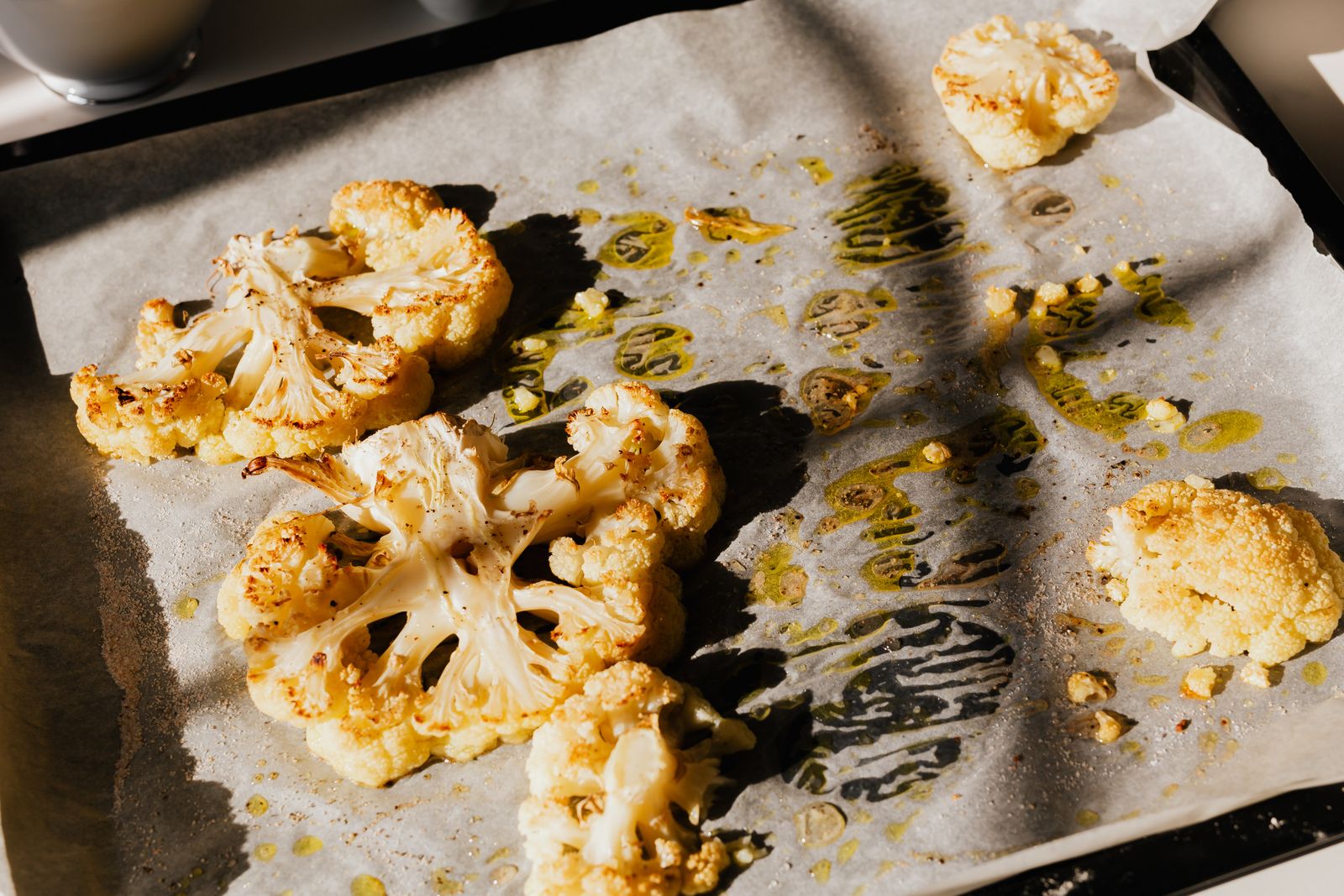 Roasted cauliflower slices on baking paper with herbs and olive oil