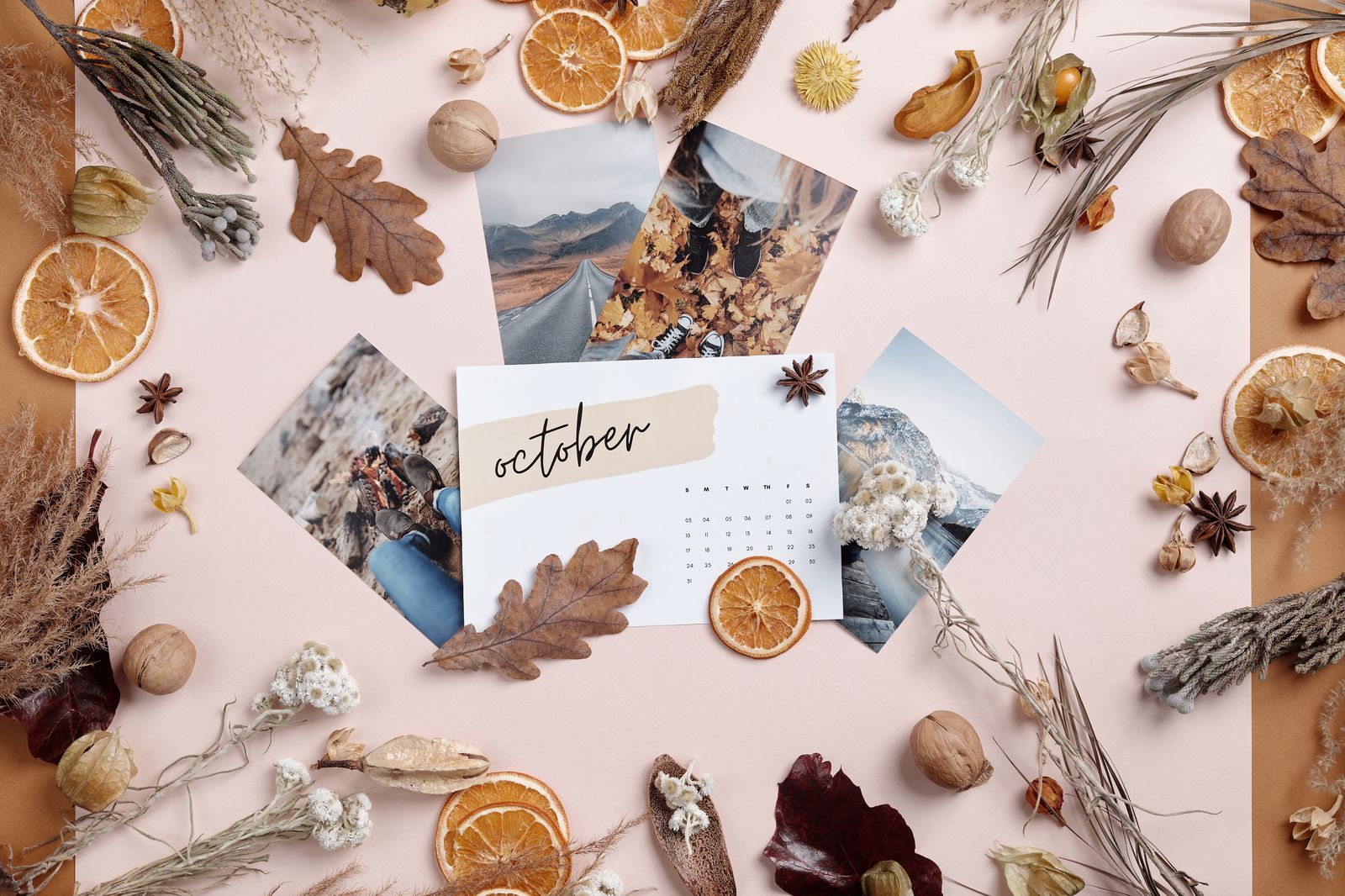 A small October calendar card on a pink table surrounded by dried leaves, orange slices and star anise