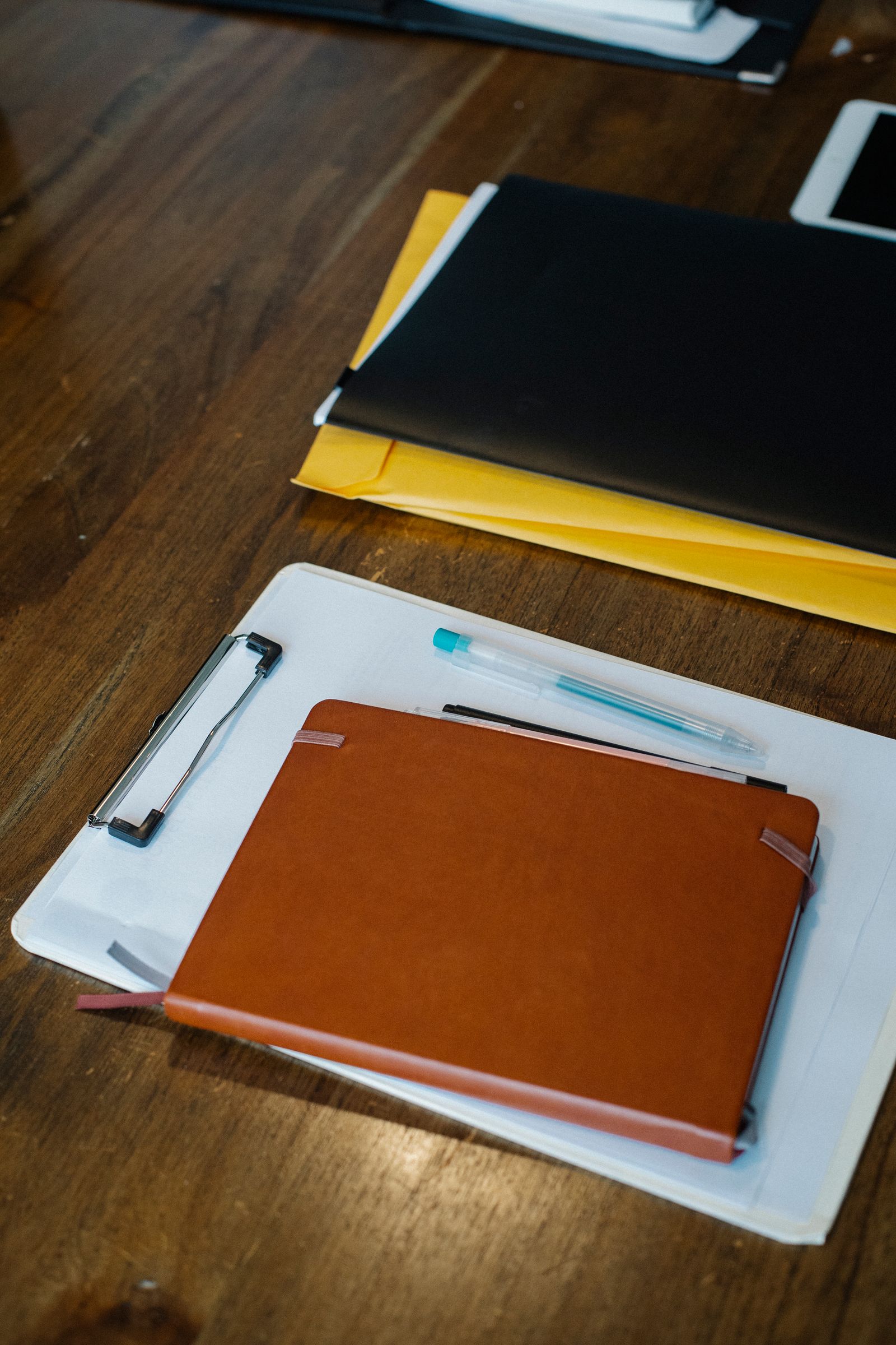 A leather notebook on a clipboard with papers and folders on a wooden desk