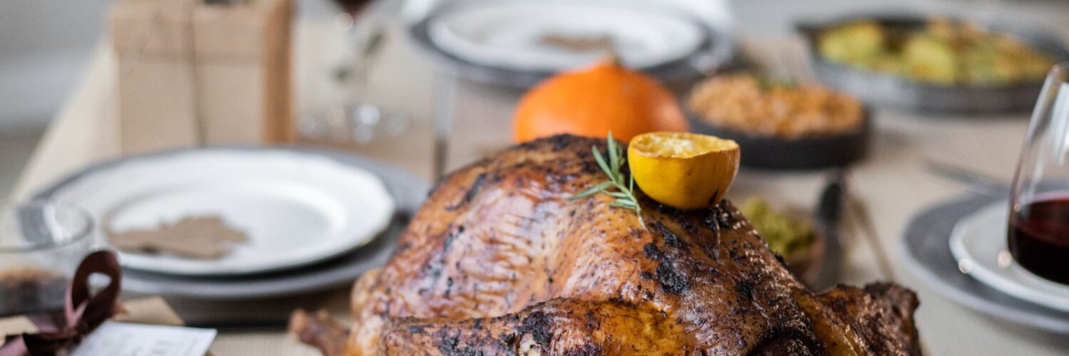 A wooden table set with a roast turkey, green vegetable sides and plates for a Thanksgiving dinner