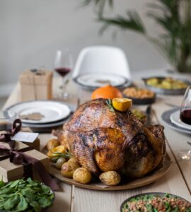 A wooden table set with a roast turkey, green vegetable sides and plates for a Thanksgiving dinner
