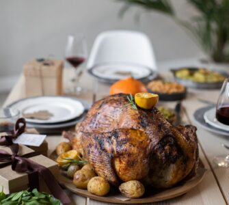 A wooden table set with a roast turkey, green vegetable sides and plates for a Thanksgiving dinner