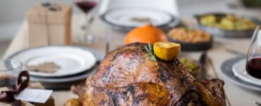 A wooden table set with a roast turkey, green vegetable sides and plates for a Thanksgiving dinner