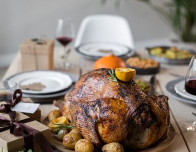 A wooden table set with a roast turkey, green vegetable sides and plates for a Thanksgiving dinner