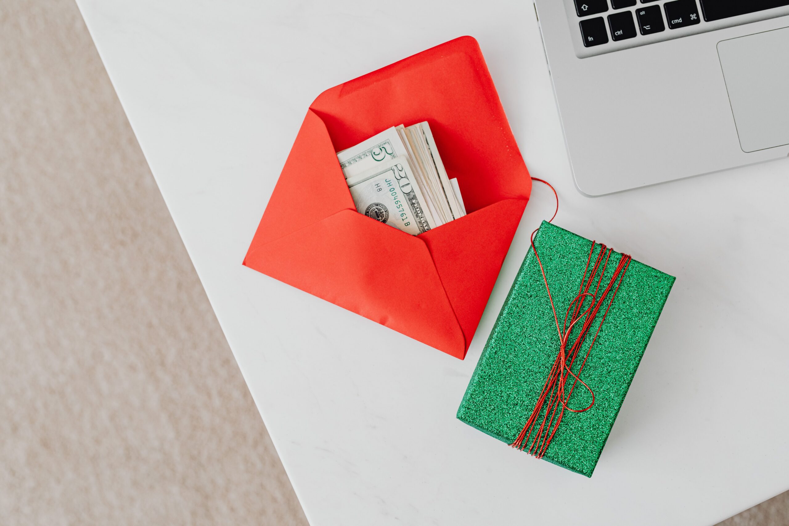 Folded cash in an open red envelope next to a green wrapped gift box on a white table