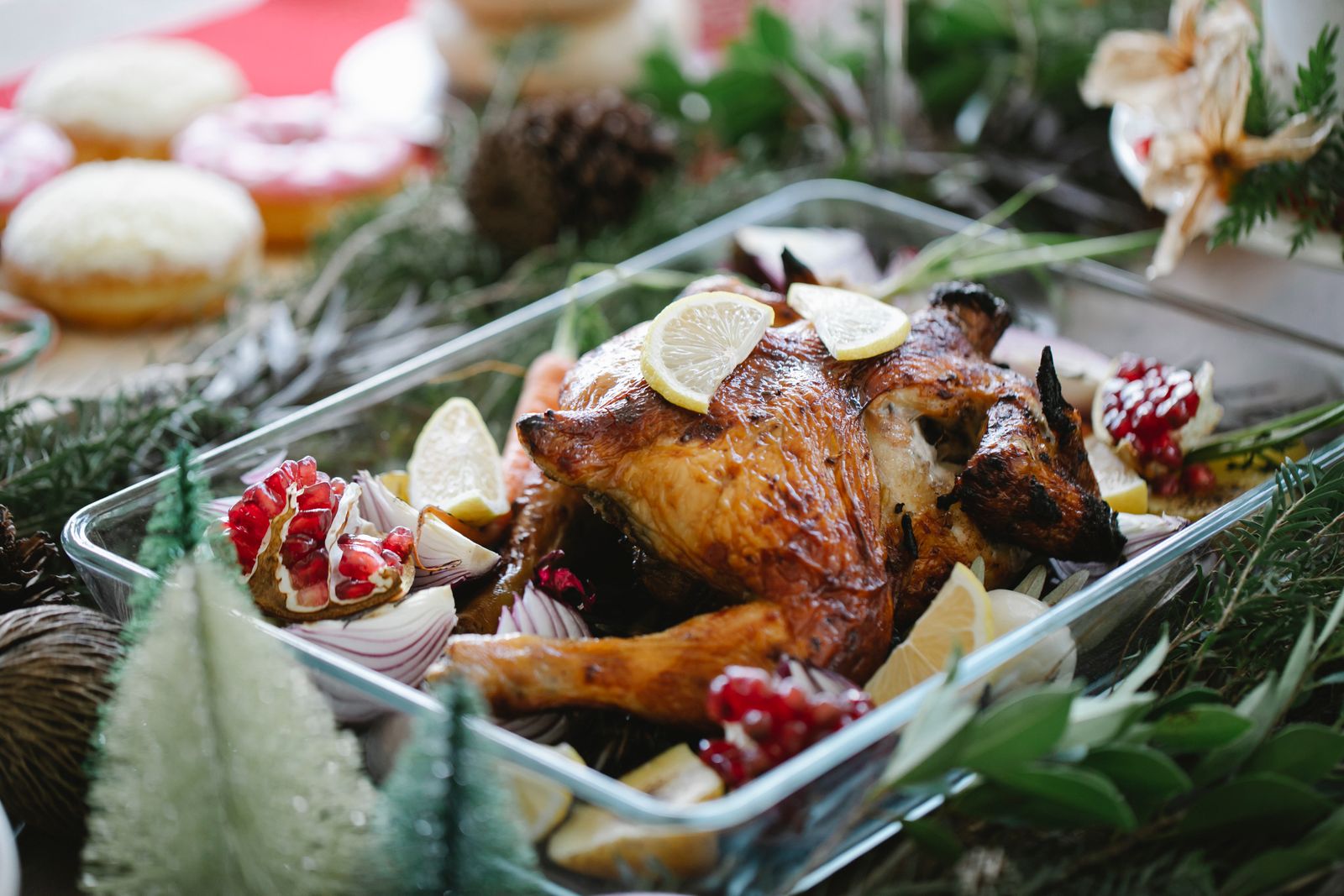 A roasted bird in a glass baking dish with lemon slices, red onion and pomegranate seeds