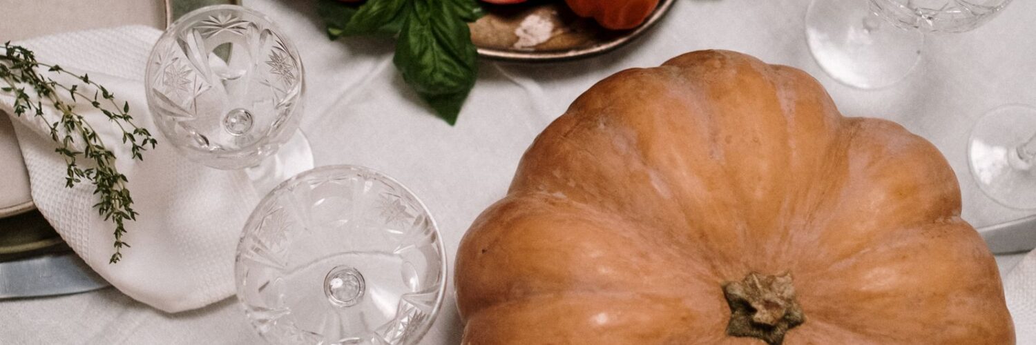 A roasted turkey on a platter beside a pumpkin on a set dinner table