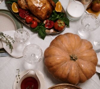 A roasted turkey on a platter beside a pumpkin on a set dinner table