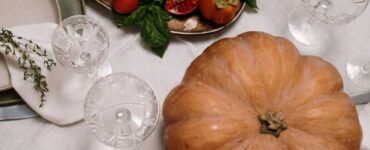 A roasted turkey on a platter beside a pumpkin on a set dinner table