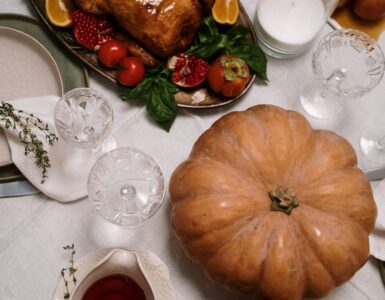 A roasted turkey on a platter beside a pumpkin on a set dinner table