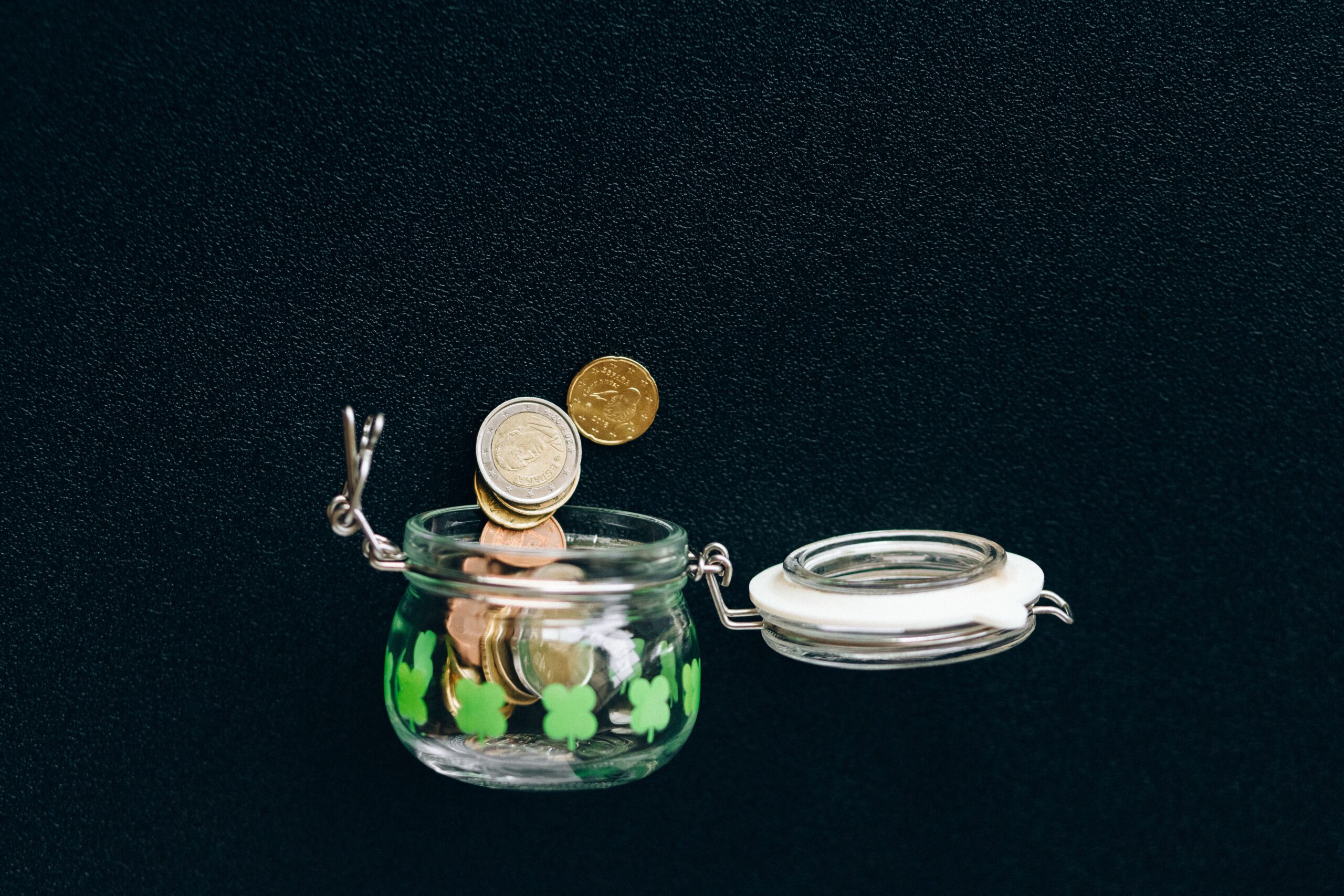 Coins dropping into an open glass jar on a dark background