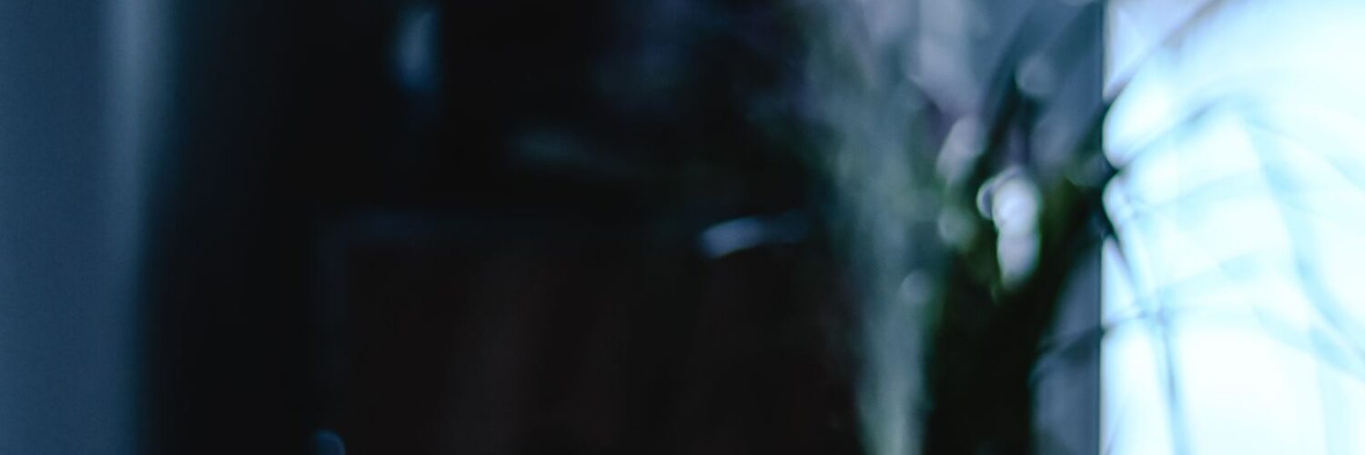 A small tabletop mist unit glowing on a wooden table beside a window, releasing a thin plume of vapor