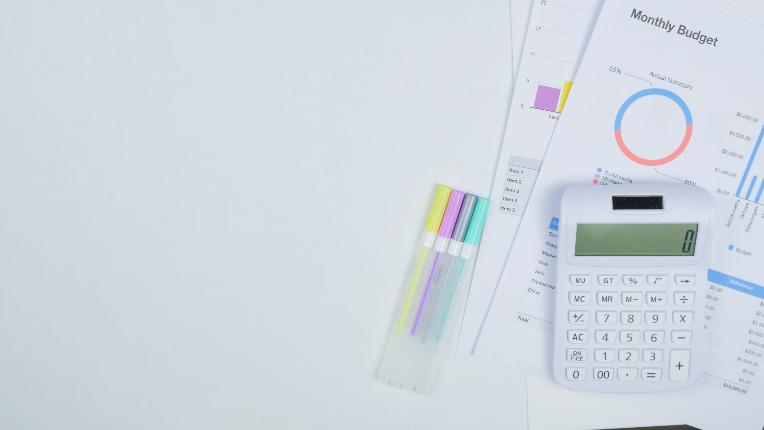 White calculator and colored pens lying on printed monthly budget sheets with a chart