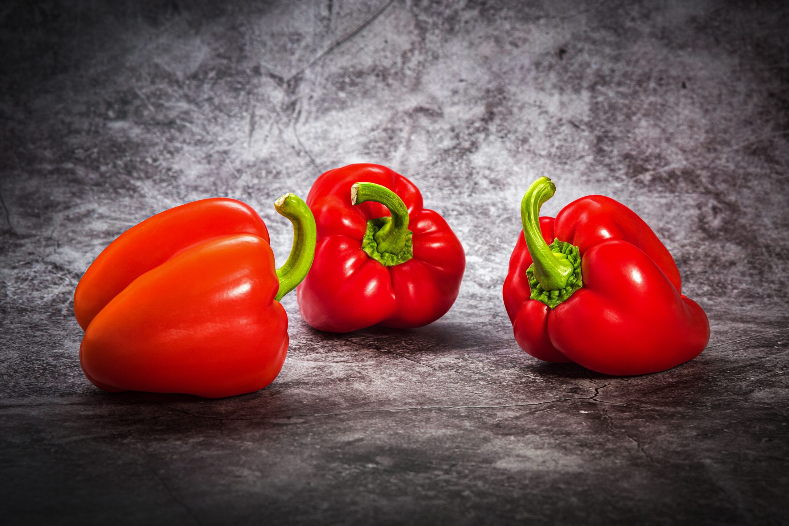 Three red bell peppers on a textured gray background