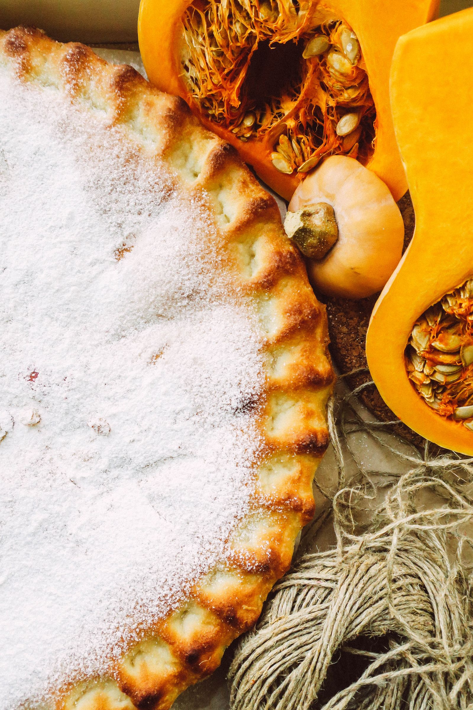 Top view of a baked pumpkin pie dusted with powdered sugar beside sliced pumpkin