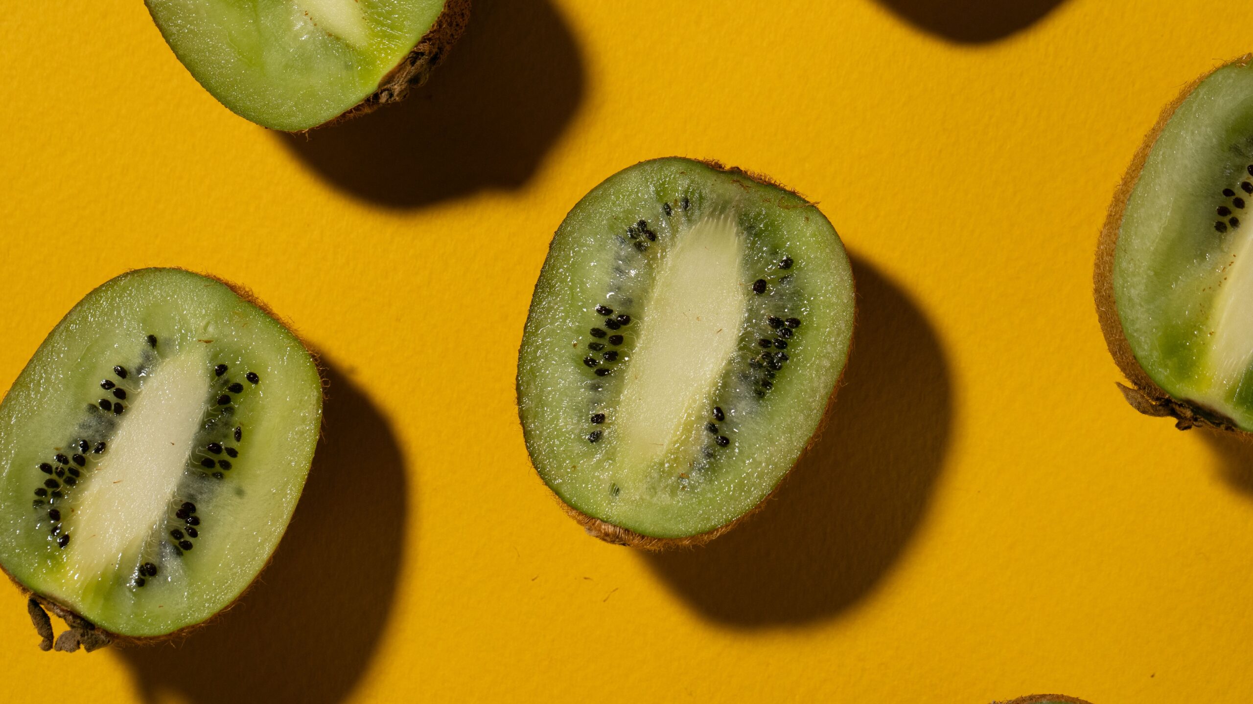 Halved kiwifruit with green flesh and black seeds on a yellow background