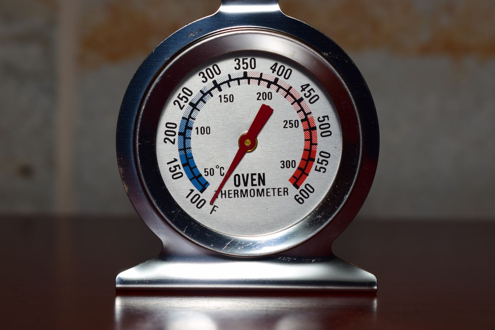 A stainless steel oven thermometer dial with Fahrenheit and Celsius scales and a red needle