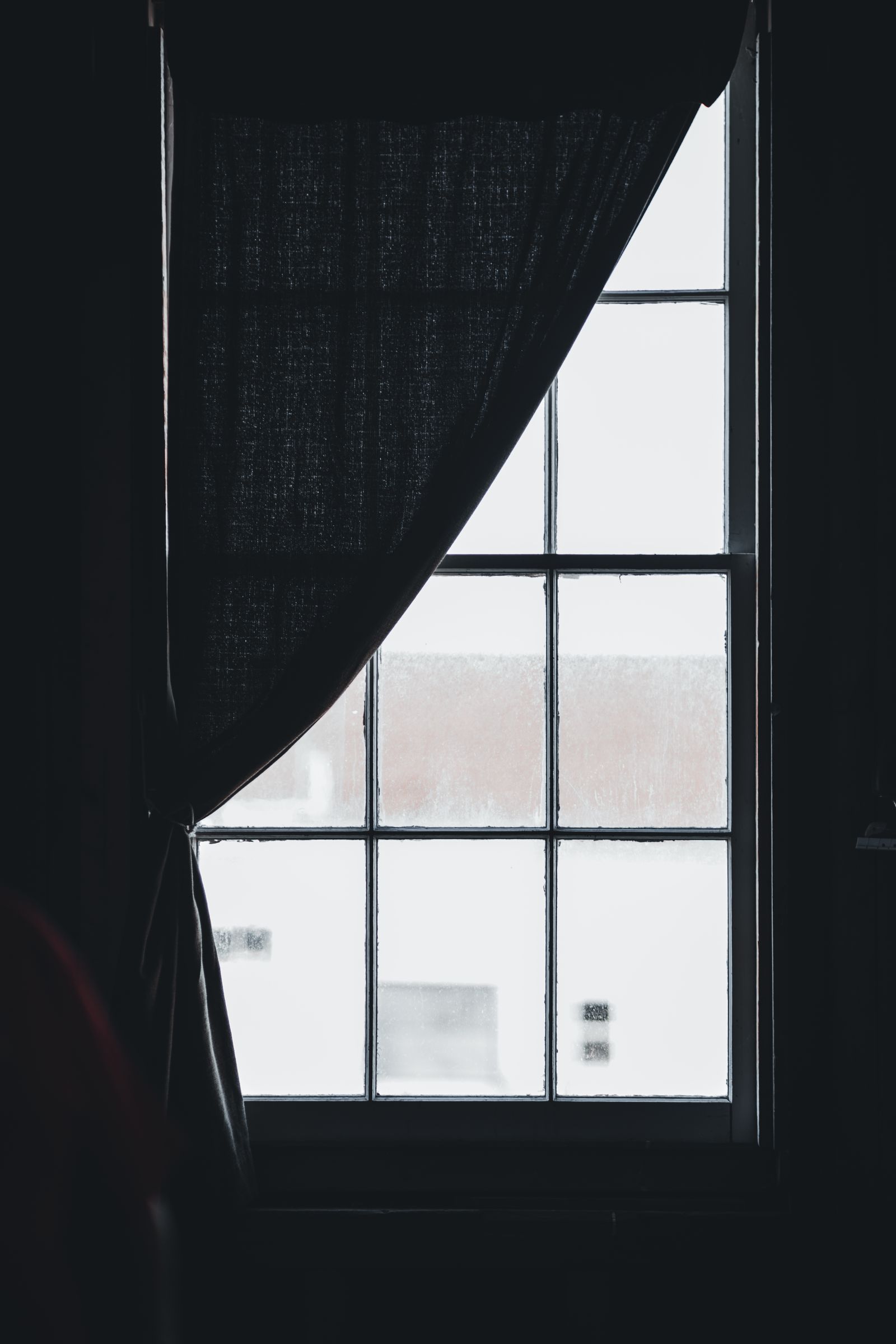 A dark curtain tied back from a tall paned window with pale winter light outside