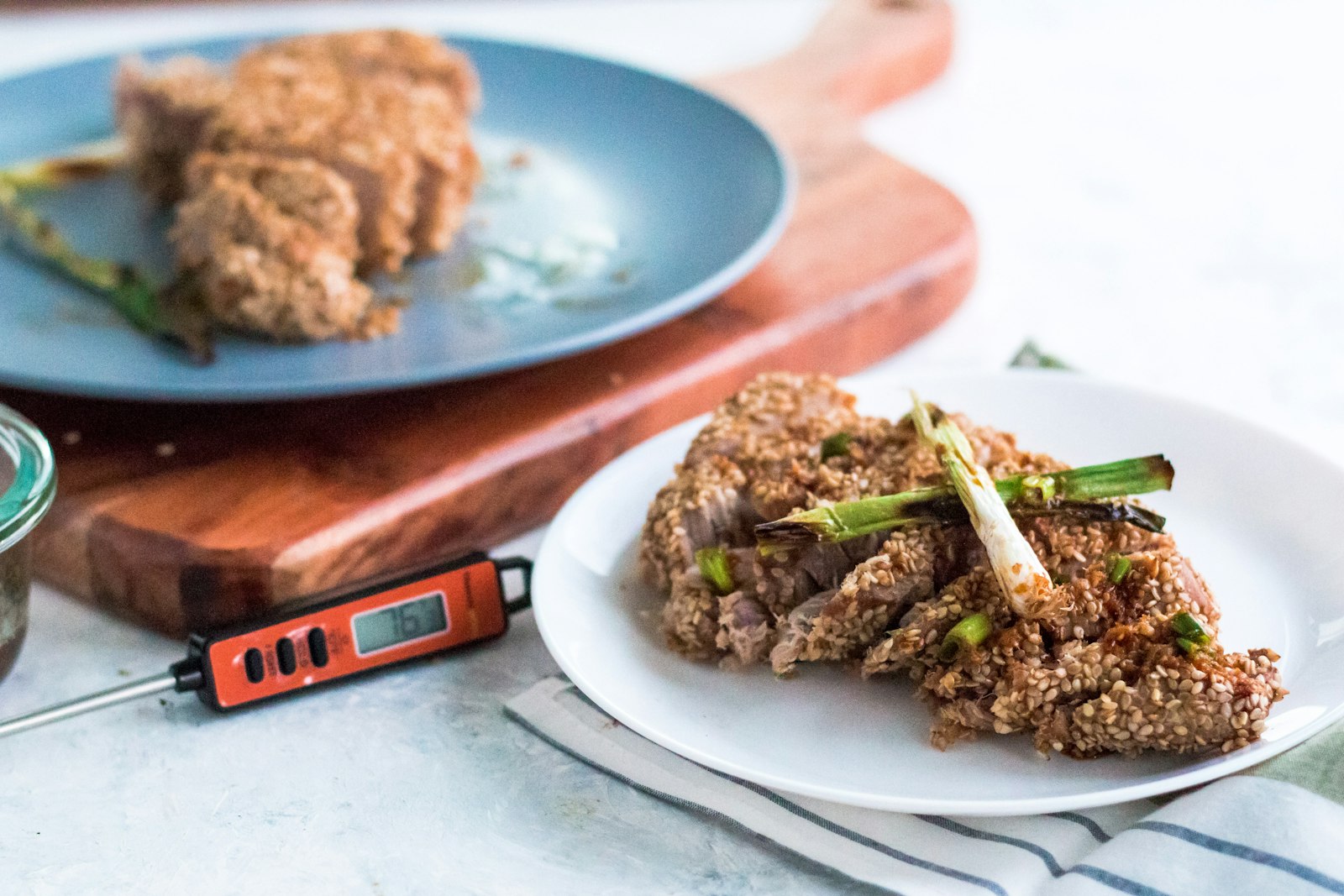 A digital food thermometer with an orange case lying on a counter beside sliced cooked meat on a plate