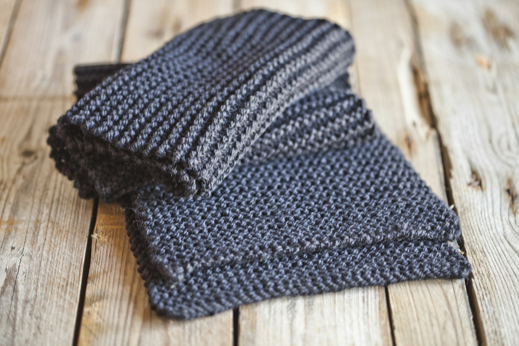 A gray knitted scarf laid out on a wooden floor