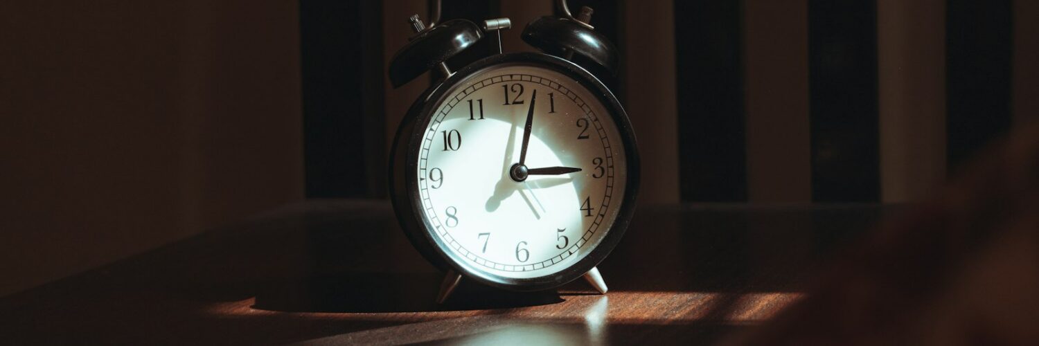 An analog alarm clock on a wooden table in a dark room at night