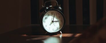 An analog alarm clock on a wooden table in a dark room at night