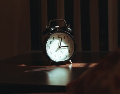 An analog alarm clock on a wooden table in a dark room at night