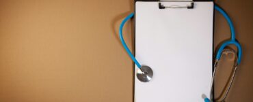 A clipboard with a stethoscope laid on top against a brown background