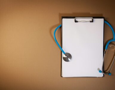 A clipboard with a stethoscope laid on top against a brown background